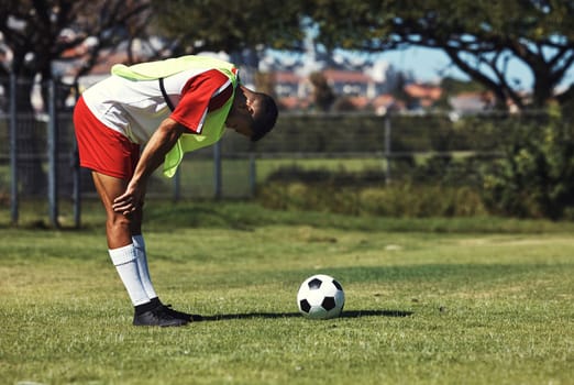 Man, tired and soccer ball on field in training, warmup or workout outdoor in summer. Exercise, soccer player and rest by football on grass in sunshine for sport, health or performance in development