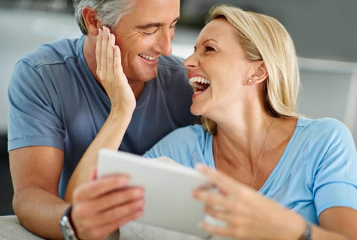 Who doesnt like a good meme. a laughing couple sitting at home using a digital tablet.