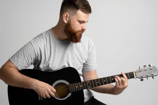 A young stylish men with a beard with a acoustic guitar on a white background. Music performer musician. Musical string instrument.