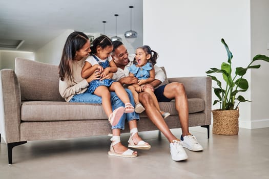 Mother, father and children laughing on sofa together, having fun and bond on weekend. Love, affection and multicultural family on couch in living room. Happy parents playing with kids in family home