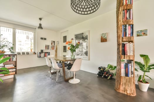 a living room with books on the shelves and plants in vases next to the dining table that is white
