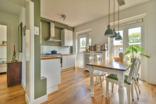 a kitchen and dining area in a house with wood floors, white cabinets, green walls and an open door leading to the patio
