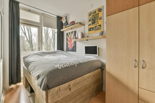 a bedroom with a bed and cupboards on the wall next to it is a window that looks out onto trees