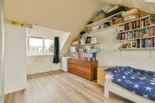 Amsterdam, Netherlands - 10 April, 2021: a bedroom with a bed and bookshels on the shelf above it in an attic style room that has been used for storage