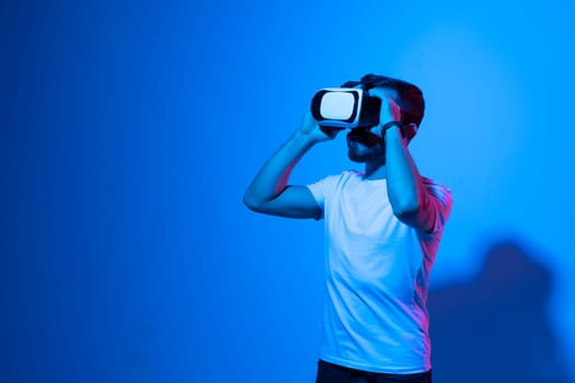 Portrait of young man with 3D virtual reality glasses enjoys his trip in an adventurous world in neon light. Concept of connection technology with science, augmented reality.