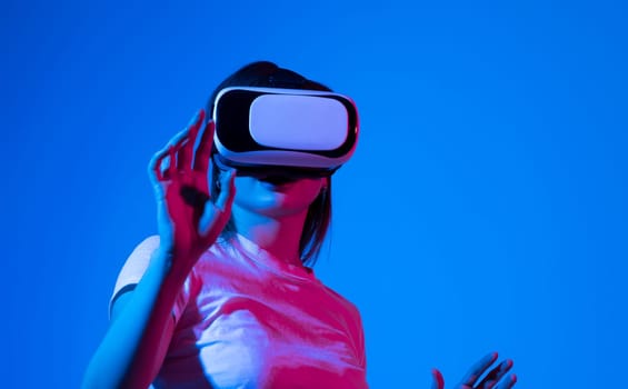 Woman in white shirt wearing VR glassess, VR set equipment for exploring a metaverse. Girl wearing a VR headset and interacting with virtual reality. Simulation, AR and metaverse concept.