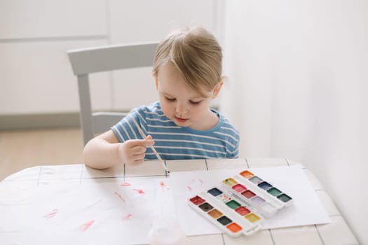 Child painting and drawing with watercolor paint at white table. Development of creative potential in children. quarantine, homeschooling concept