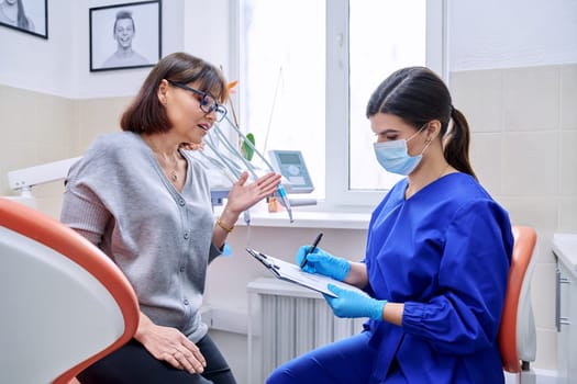 Dental office visit, female patient talking to doctor, dentist making notes for patient treatment. Treatment, dental care, prosthetics, orthodontics, dentistry concept