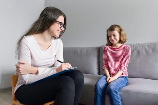 Professional child psychologist talking with child girl in office