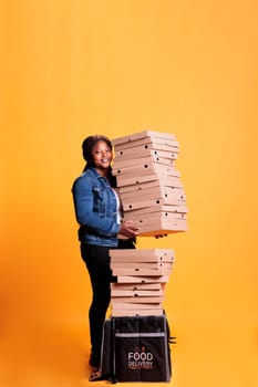 Smiling deliverywoman holding stack full of pizza boxes preparing to deliver to clients