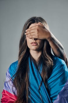Surprise, cover and woman with bisexual flag isolated on a grey studio background. Love, freedom and girl in support of LGBT community with person covering eyes to be surprised for pride on backdrop