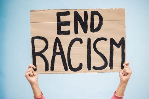 Hands, cardboard poster and end racism for protest, march or community advertisement against studio background. Hand of activist holding billboard, banner or sign for equality, message or protesting