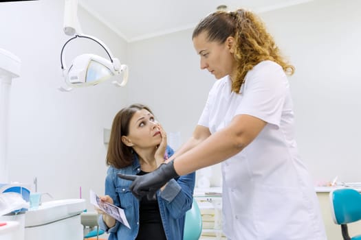 Mature woman with toothache talking to professional dentist, females looking x-ray, doctor advising patient and recommending treatment