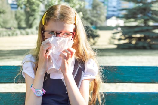 Little girl sitting in park sneezing with handkerchief, seasonal allergies