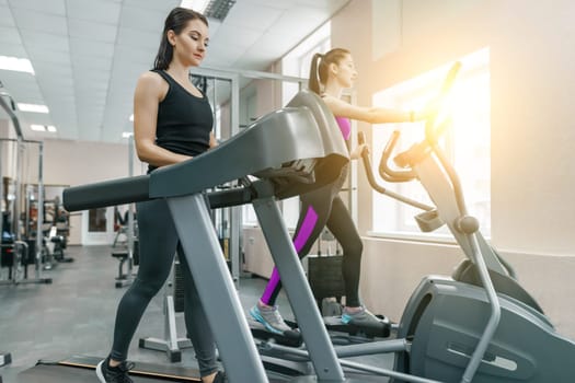 Two young fitness healthy women on treadmill in sport modern gym. Fitness, sport, training, people concept