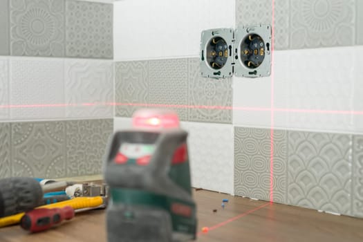 Electrician using infrared laser level to install electrical outlets.