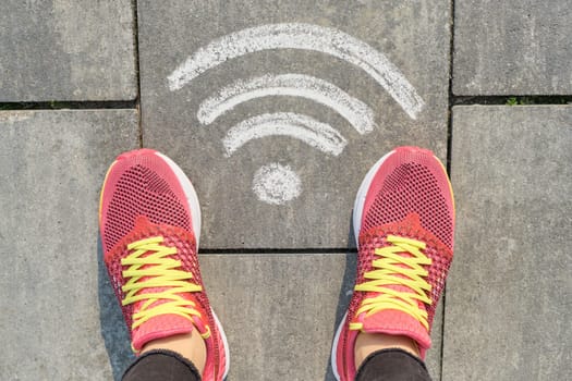 Wi-fi symbol on gray sidewalk with woman legs in sneakers, top view