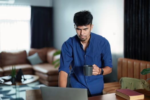 Portrait of an Asian man working on a computer and drinking coffee