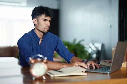 Portrait of an Asian man using a computer and note book to record his work