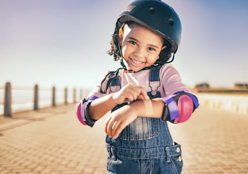 Skating injury, first aid or child portrait with bandage bruise from skate, cycling or accident in street. Happy, smile or girl with helmet for exercise, wellness health at beach, sea or ocean