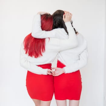 Rear view of two women dressed in identical red dresses and white sweaters. Lesbian intimacy. White background.