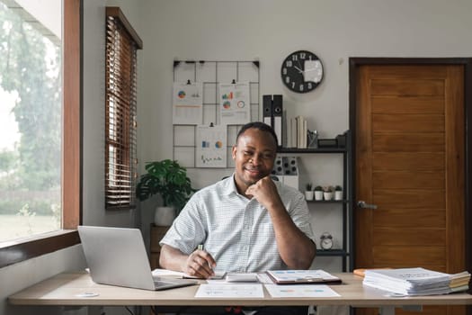 Happy black man planning budget, calculating expenses and taking notes in planner at home