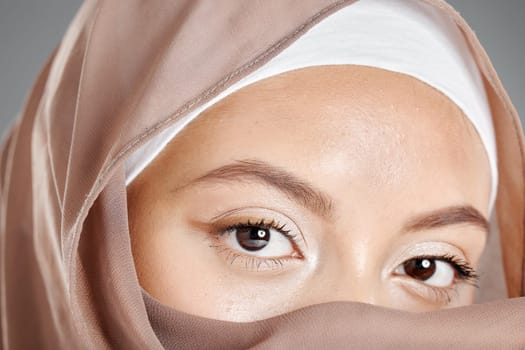Muslim, eye and beauty with face of woman for health lashes, makeup and vision in grey background. Youth, cosmetics and skincare with islamic girl and zoom in stare for hijab, serious or religion