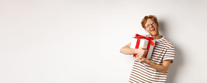 Valentines day and holidays concept. Happy redhead man hugging his gift box and thanking, looking at camera excited and grateful, white background
