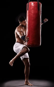 Martial arts is not about fighting its about building character. Studio shot of kick boxer working out with a punching bag against a black background.