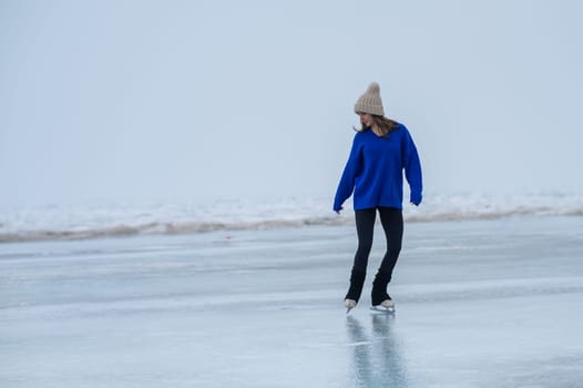 Caucasian woman in a blue sweater skating on a frozen lake.