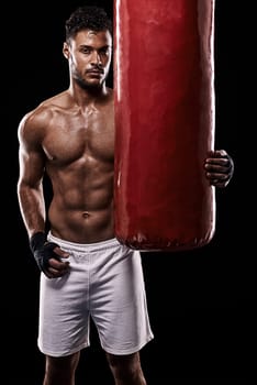 Train hard and be the best. Studio shot of kick boxer working out with a punching bag against a black background.