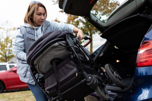 mom driver puts baby stroller in car trunk