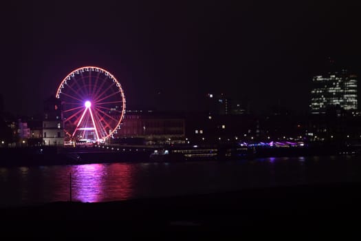 Rhine riverbank by night with castle tower and Ferris pink wheel in Duesseldorf, Germany