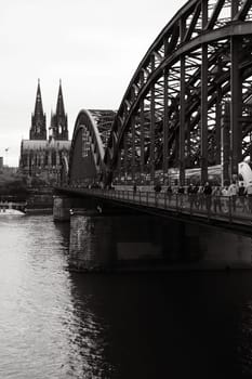 Greyscale shot of the Cologne Cathedral and the Hohenzollern Bridge at dusk