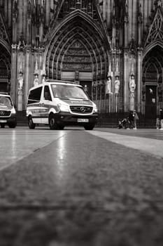Grayscale shot of Mercedes-Benz Sprinter police car in front of Cologne Cathedral in Germany