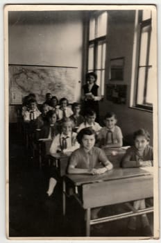 Vintage photo shows pupil sit at the school desk in classroom.