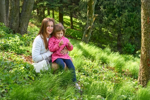 Pretty mother with a cute child walk in the forest park studying nature