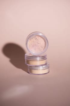 Mineral powder for skin tone color in small containers on pale rose colour background with shadows - beauty product and make up concept