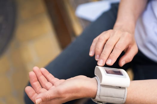 Close-up of elderly woman's hands holding pressure measurement device outdoors. The image portrays the concept of health monitoring, diagnosis, and healthcare for seniors.