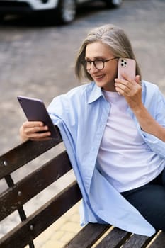 Happy senior woman is multitasking with a tablet PC and phone call on a busy city street. She showcases modern technology and active lifestyle in the elderly population.