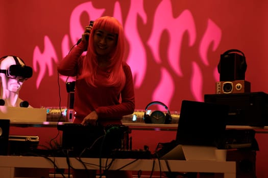 Asian woman with pink hair mixing techno music on turntables while playing record mix sounds in studio