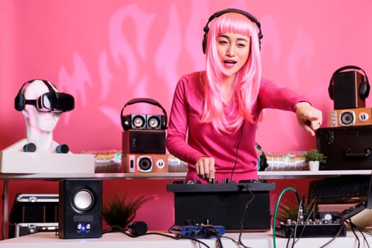 Asian performer wearing headphones while playing electronic music using professional mixer console