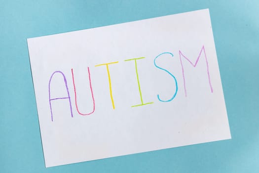 Text word autism on paper sheet written by colorful letter, on blue background.