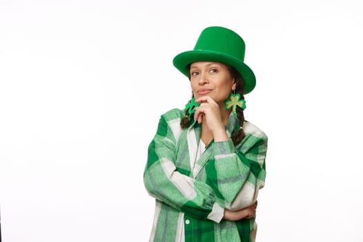 Pensive woman in carnival green hat and clover leaf earrings on white background. Saint Patrick's Day. Irish culture
