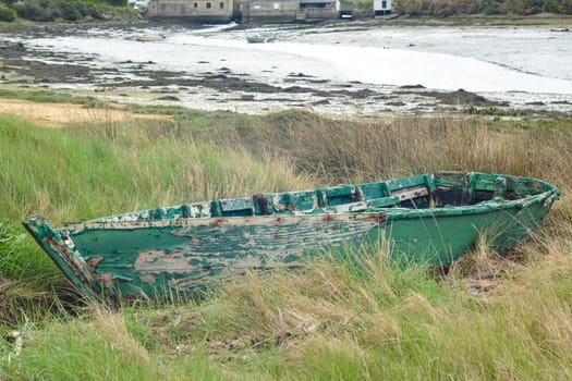 A green abandoned boat at a coast