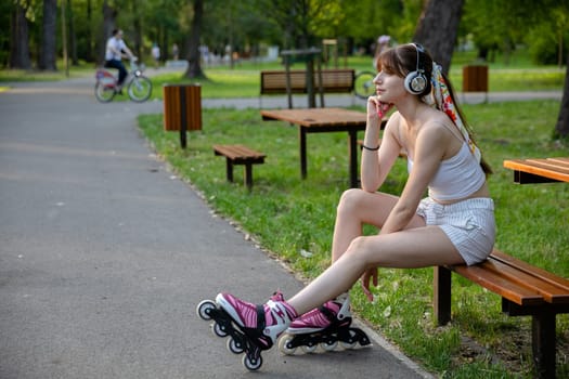A girl wearing rollerblades sits on a bench by an alley