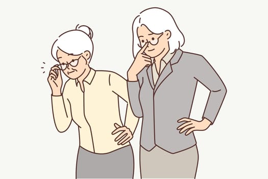Two elderly women in business clothes carefully look to side watching work of young employees