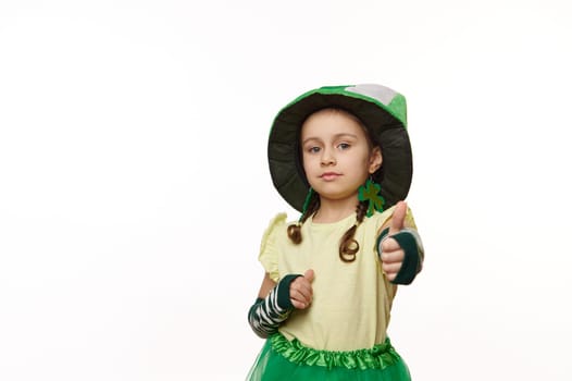 Lovely Irish little girl dressed like Leprechaun for St Patrick Day party, shows thumb up looking at camera