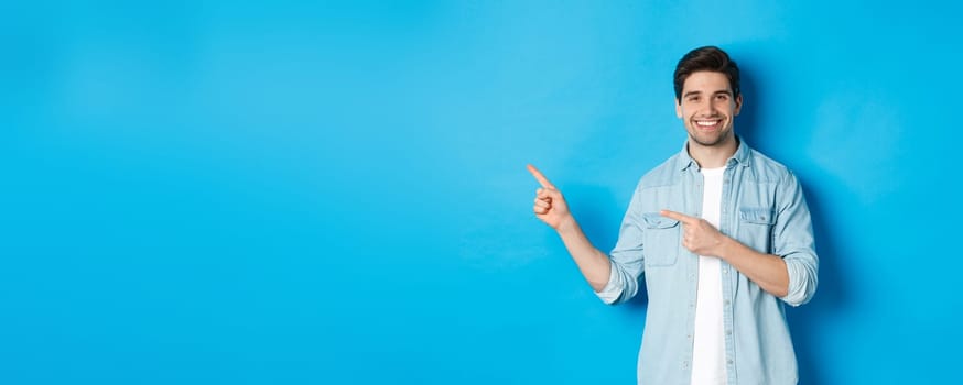 Handsome caucasian man in casual outfit, pointing fingers left and smiling, showing promo offer, standing over blue background