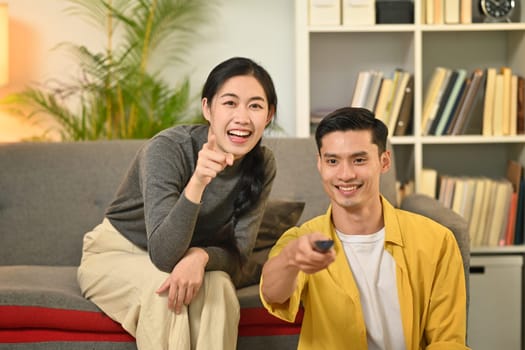 Happy young couple relaxing and watching TV together on a couch in cozy home. People and leisure activity concept